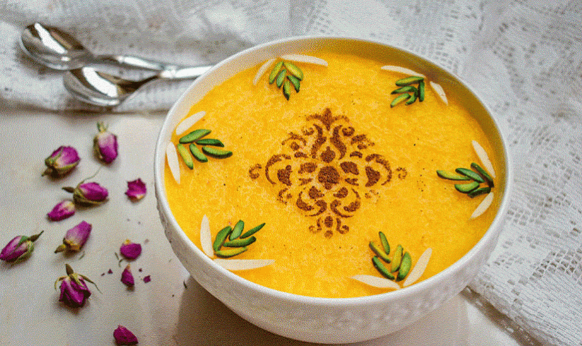 Golden sholeh zard saffron rice pudding decorated with cinnamon and pistachios in a white bowl