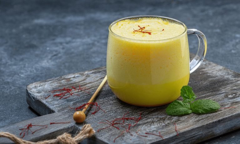 Warme Safran Milch in einer Keramiktasse mit goldgelber Farbe, zubereitet aus leicht zerstoßenen Safranfäden als ruhiges Abendritual.