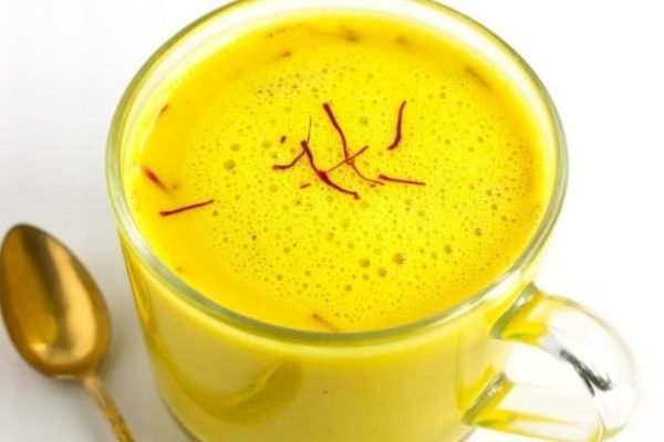 Warme Kesar Doodh in einer Keramiktasse, indische Safranmilch mit goldgelber Farbe, verfeinert mit Safranfäden als traditionelles Abendgetränk.