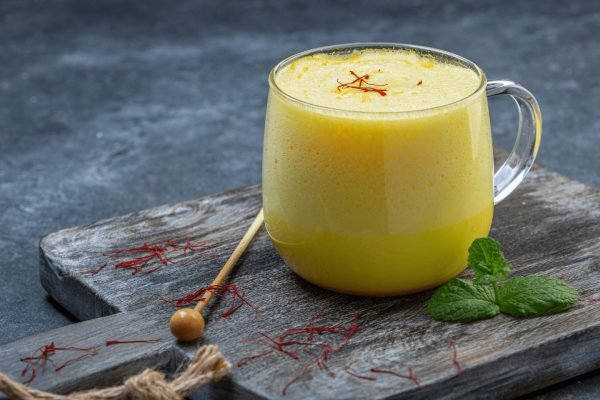 Warme Safran Milch in einer Keramiktasse mit goldgelber Farbe, zubereitet aus leicht zerstoßenen Safranfäden als ruhiges Abendritual.